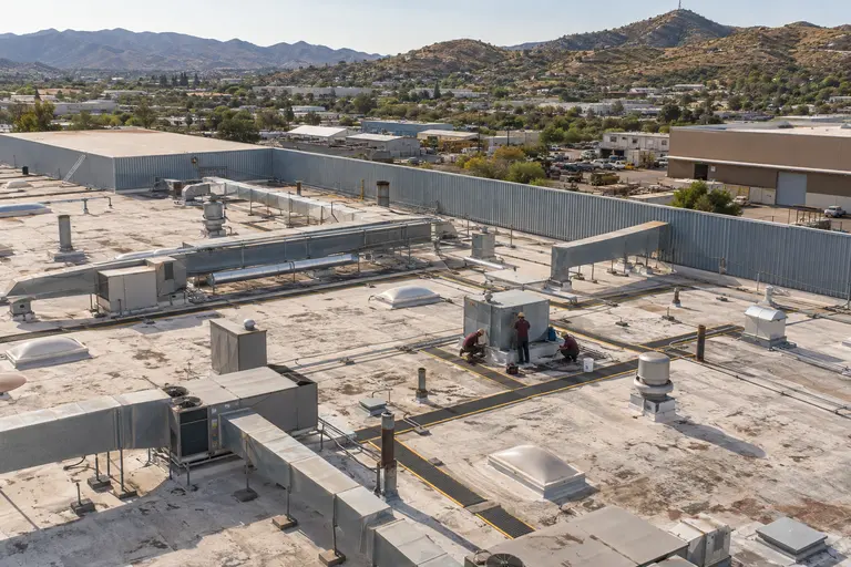 Roofers sealing a curb among ductwork and exhaust fans on an industrial roof